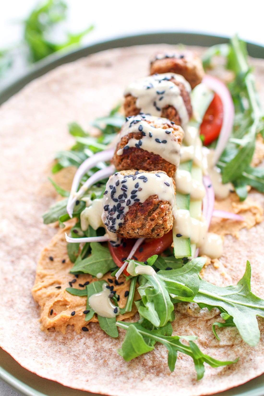 Savoury falafel, wrapped in a large tortilla smothered in red pepper hummus, topped with peppery arugula, crunchy cucumbers, tomatoes, onions and drizzled in creamy tahini. 