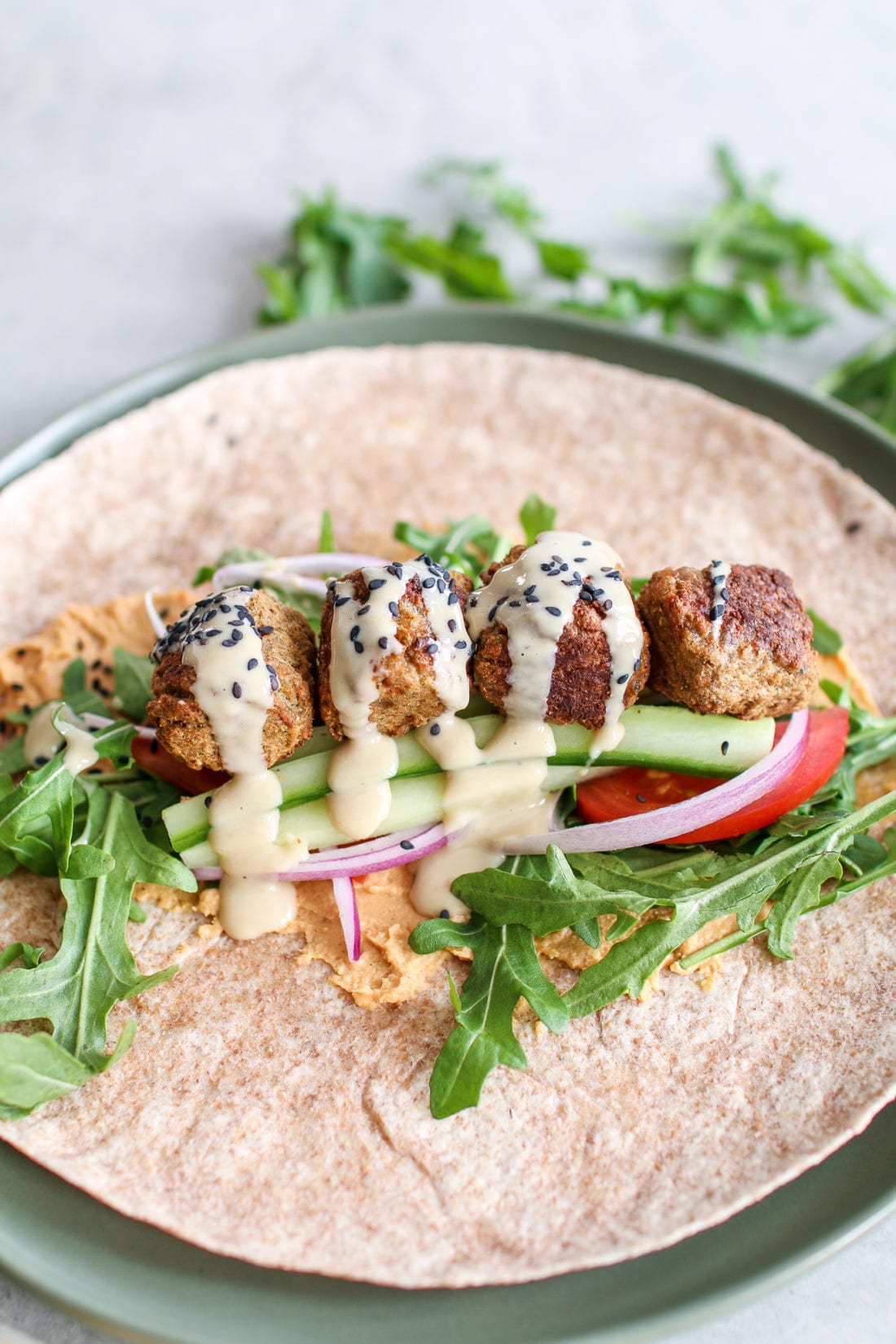 Savoury falafel, wrapped in a large tortilla smothered in red pepper hummus, topped with peppery arugula, crunchy cucumbers, tomatoes, onions and drizzled in creamy tahini. 