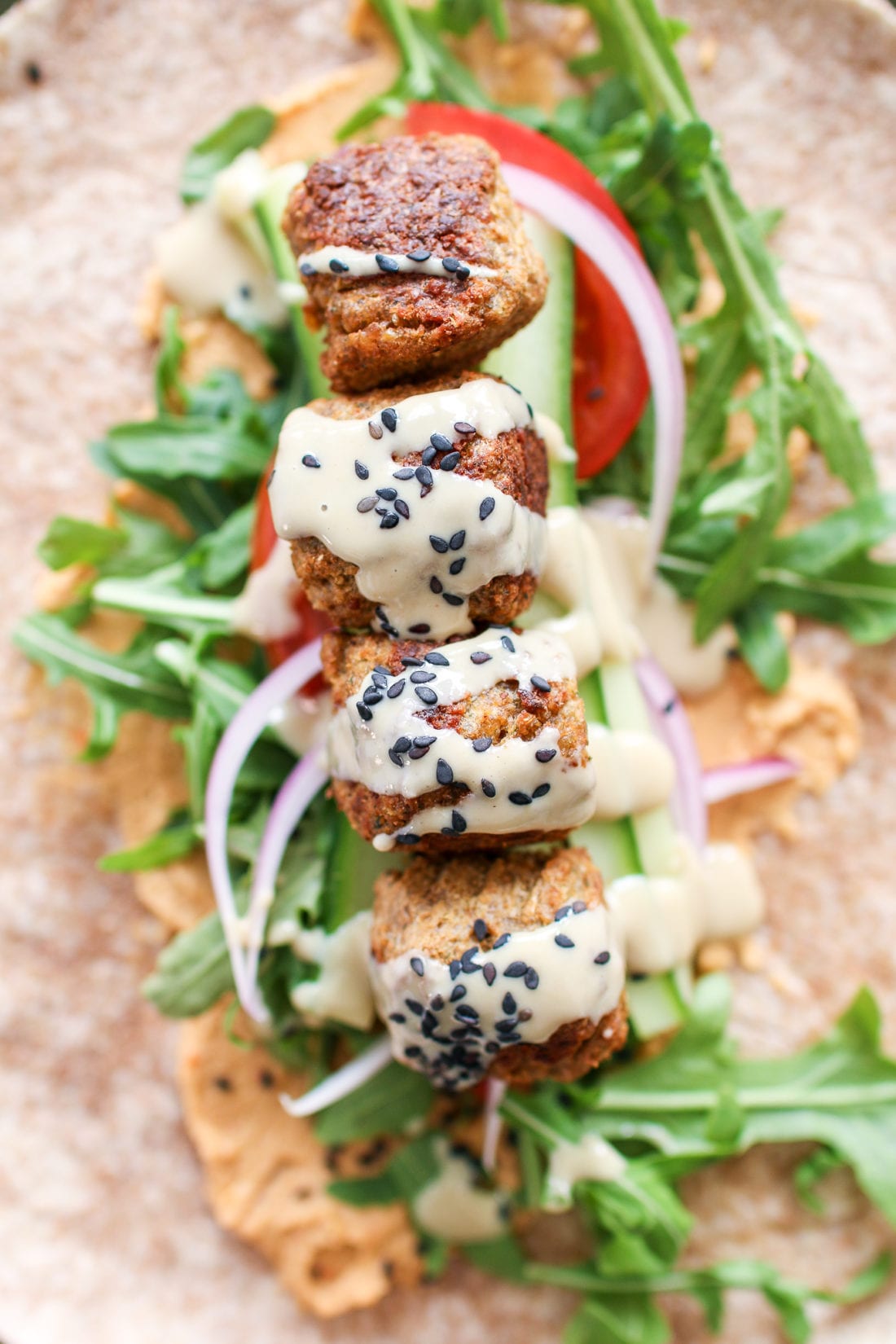 Savoury falafel, wrapped in a large tortilla smothered in red pepper hummus, topped with peppery arugula, crunchy cucumbers, tomatoes, onions and drizzled in creamy tahini. 