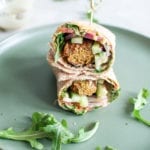 Savoury falafel, wrapped in a large tortilla smothered in red pepper hummus, topped with peppery arugula, crunchy cucumbers, tomatoes, onions and drizzled in creamy tahini.
