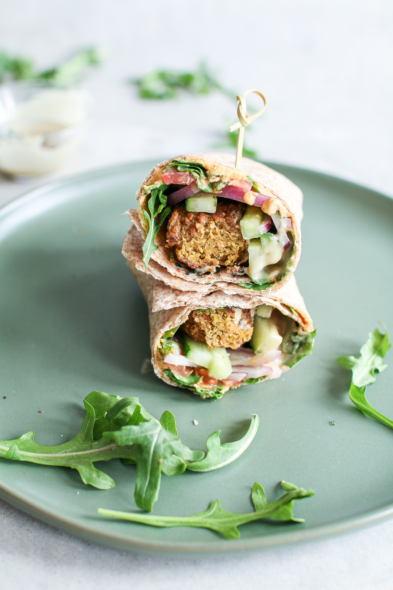 Savoury falafel, wrapped in a large tortilla smothered in red pepper hummus, topped with peppery arugula, crunchy cucumbers, tomatoes, onions and drizzled in creamy tahini.