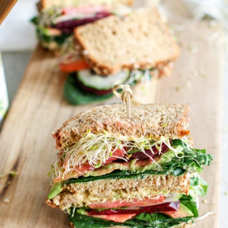A colourful veggie sandwich stacked with fresh spinach, creamy avocado, crunchy cucumbers, tomatoes, beets and microgreens, smooshed between your favourite bread and smothered in caramelized onion hummus and creamy aioli. The ultimate sammy!