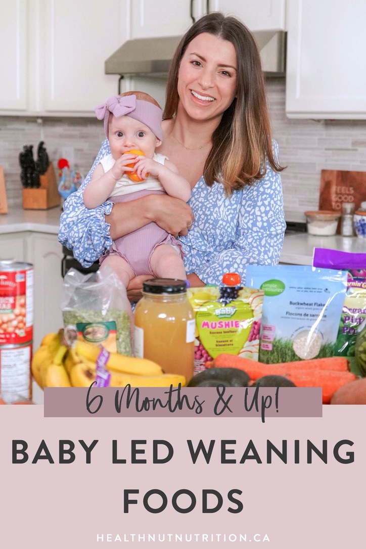 Brunette woman holding her 7 month old baby and showing off baby led weaning foods in her kitchen