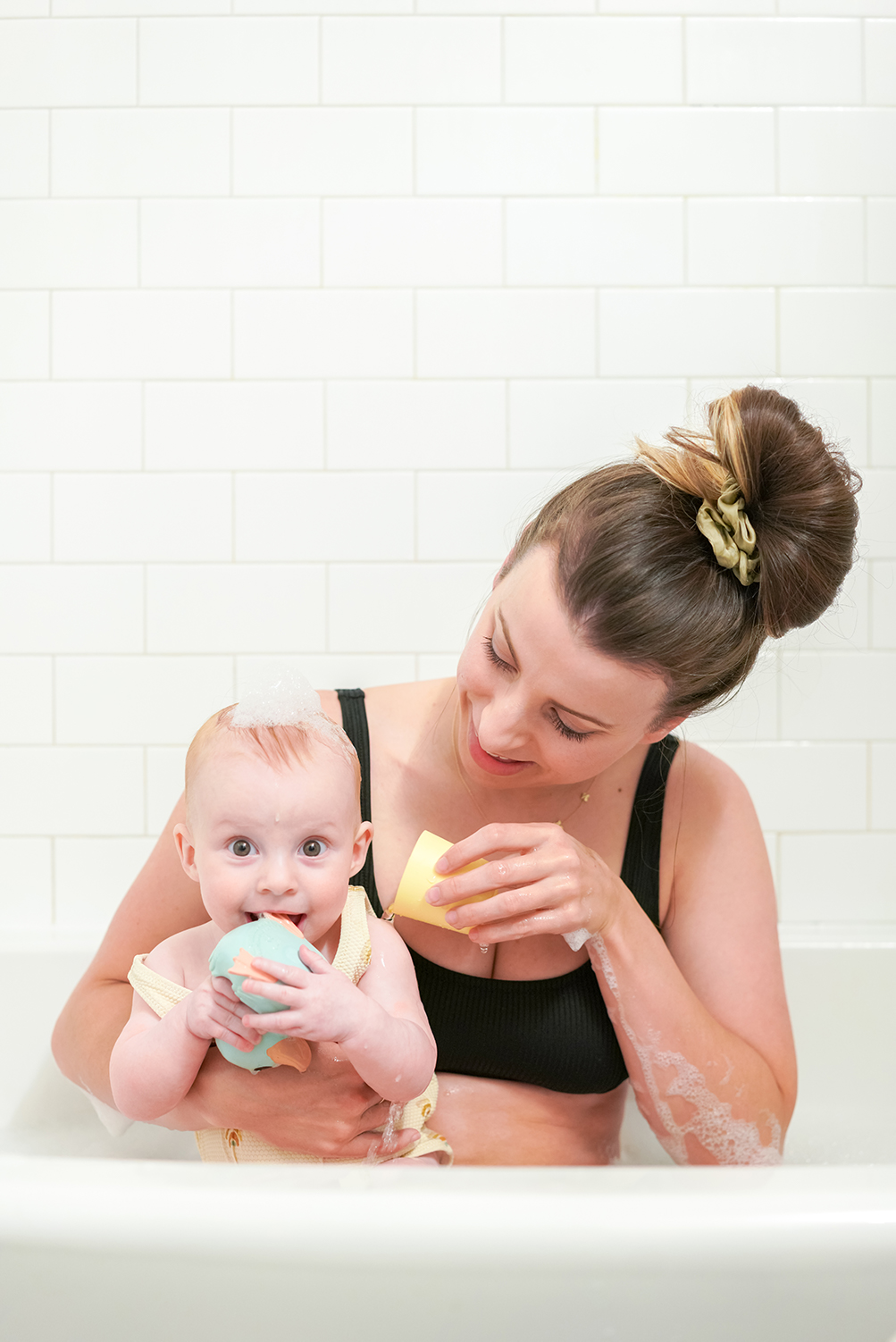 a brown haired mother bathing with her baby in a swimming costume