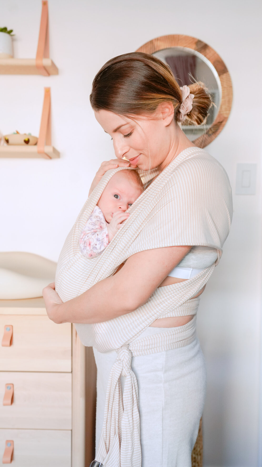 a brunette mother holding her newborn baby in a wrap