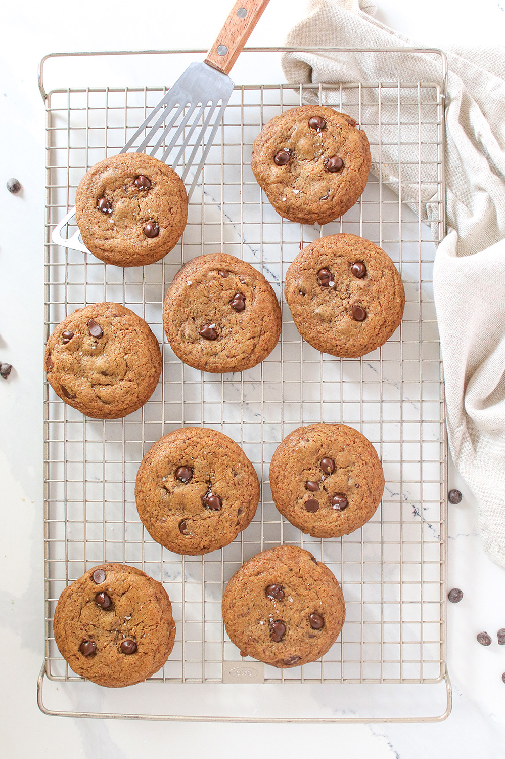 9 chocolate chip cookies on a wire cooing rack with a spatula picking one up