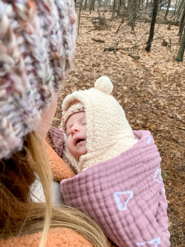 a 4-6 month old baby wrapped up in a fluffy coat and blanket, sleeping in her mother's arms