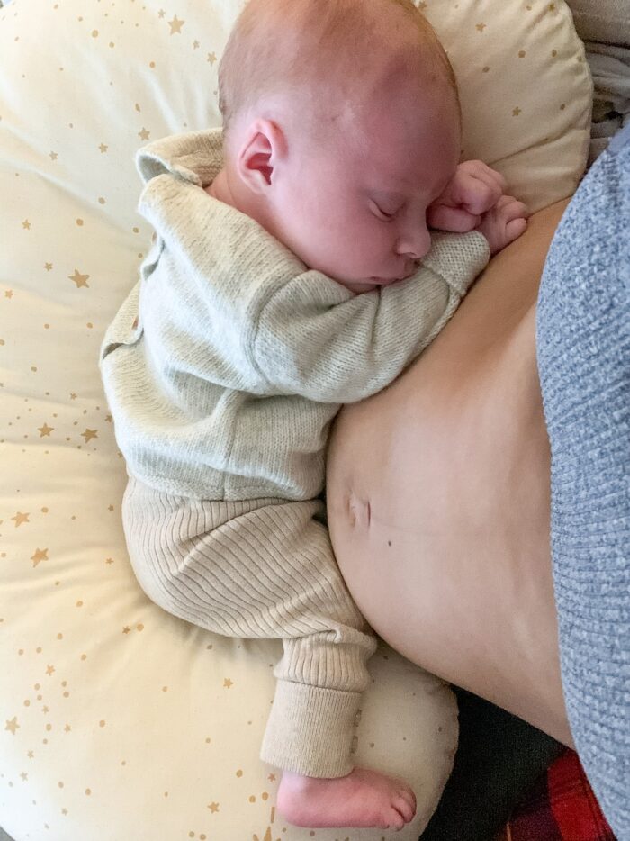 a newborn baby in a cream onesie cuddled up to her mother's stomach