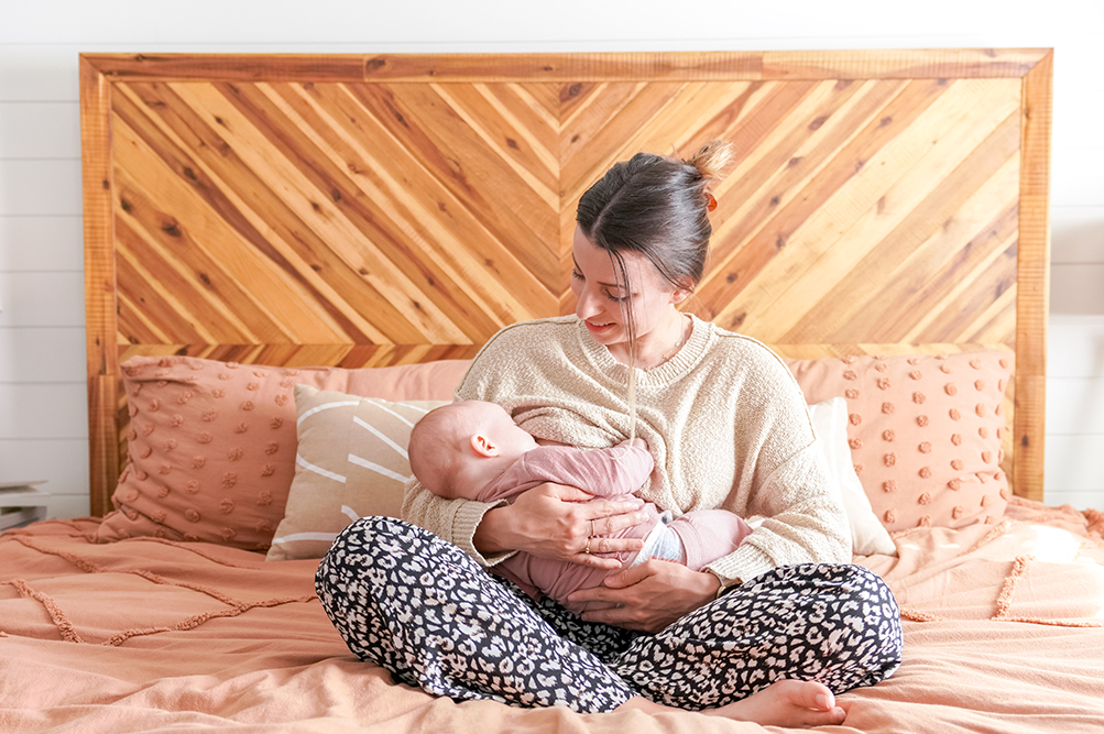 woman sitting cross legged on the bed breastfeeding her baby