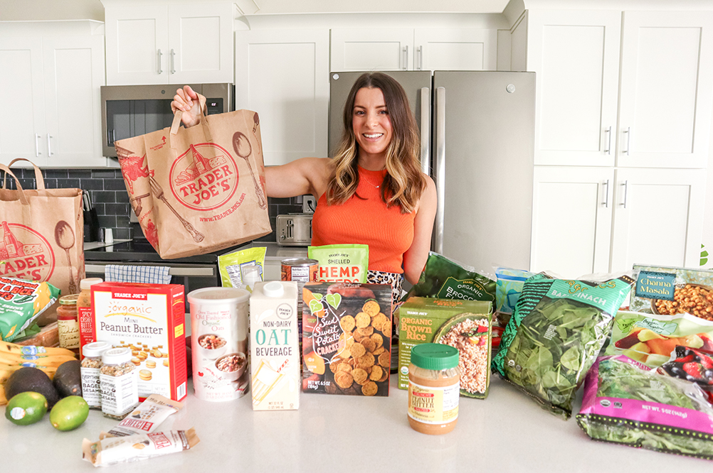 brunette woman standing in a kitchen holding up a trader joe's bag