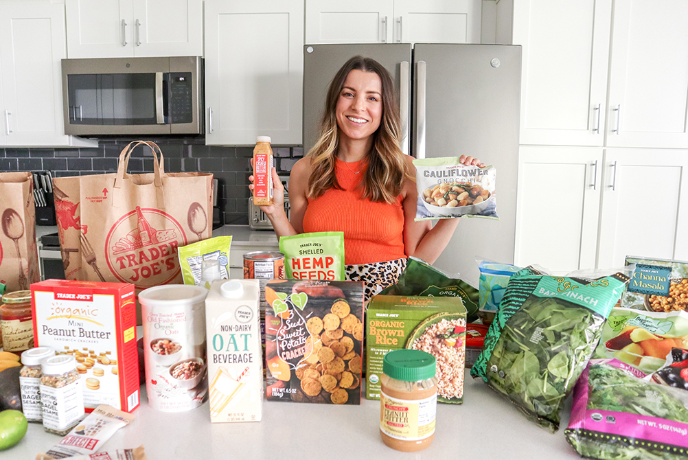 brunette woman standing in a kitchen holding up a trader joe's bag