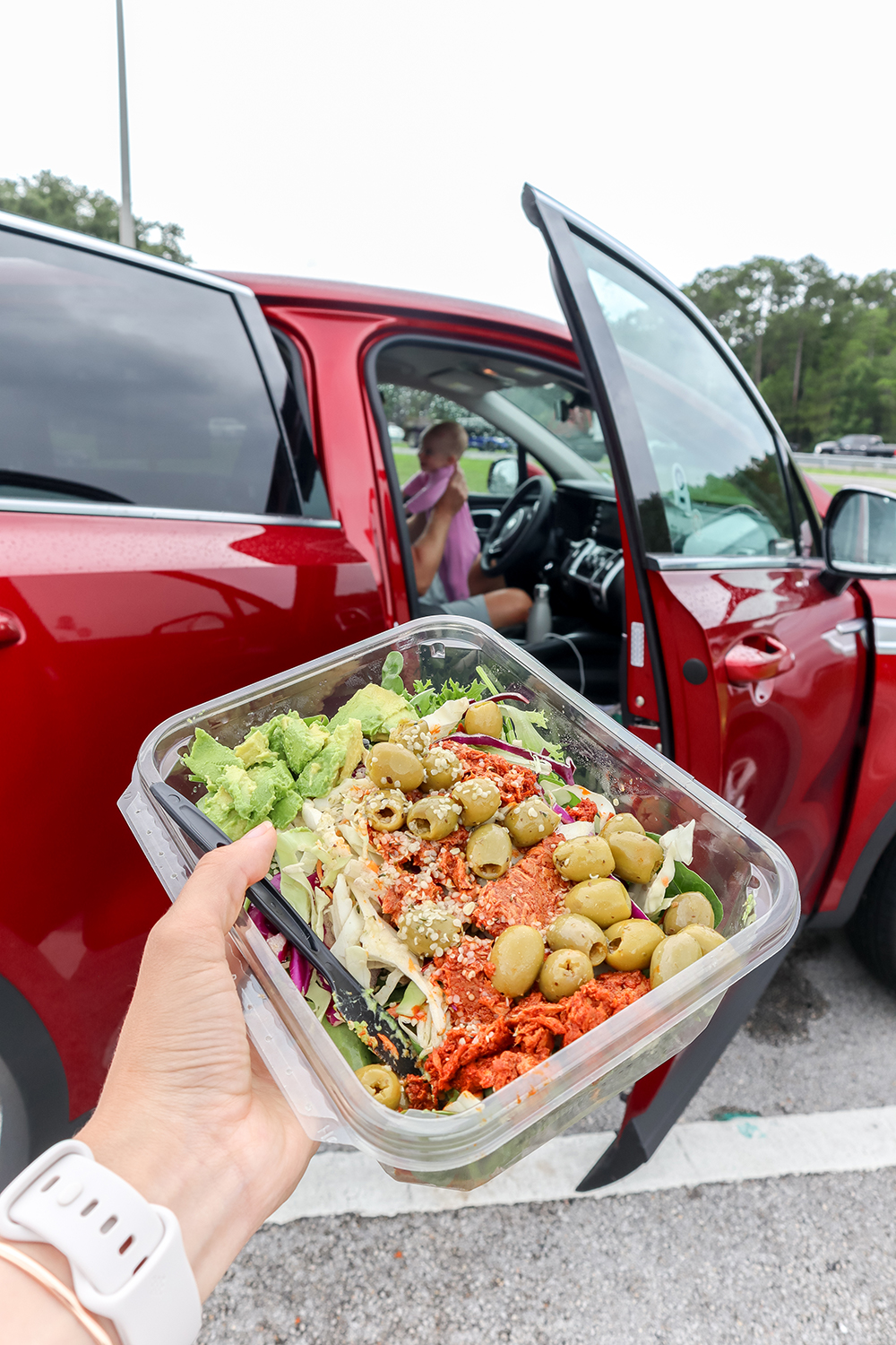 a hand holding a tuna salad in front of a car