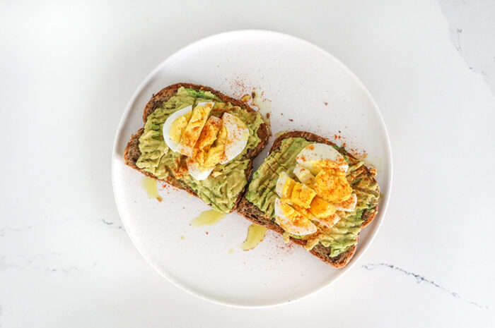 a white plate of avocado egg toast on a white counter