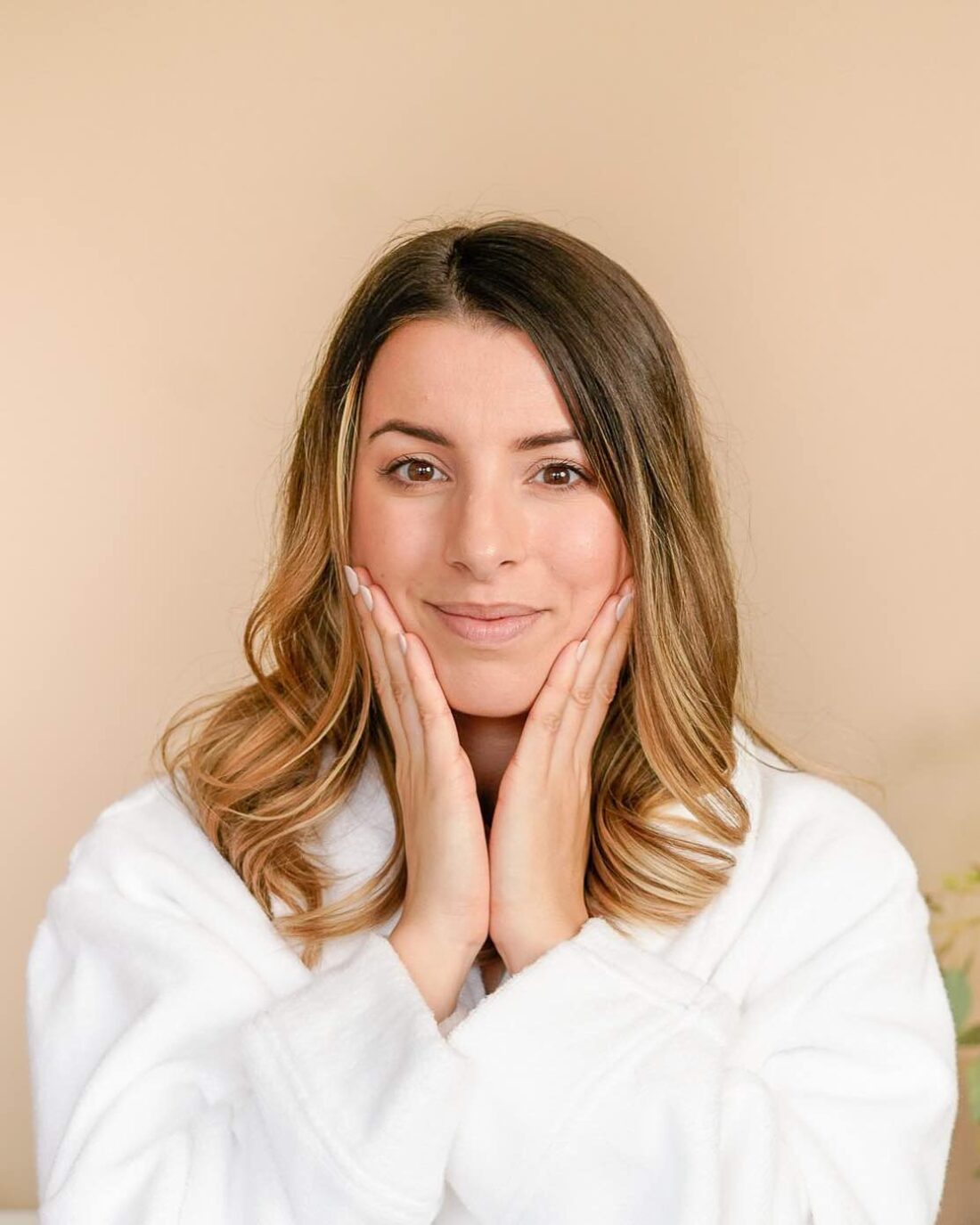 woman wearing a white dressing gown pressing her hands to her face