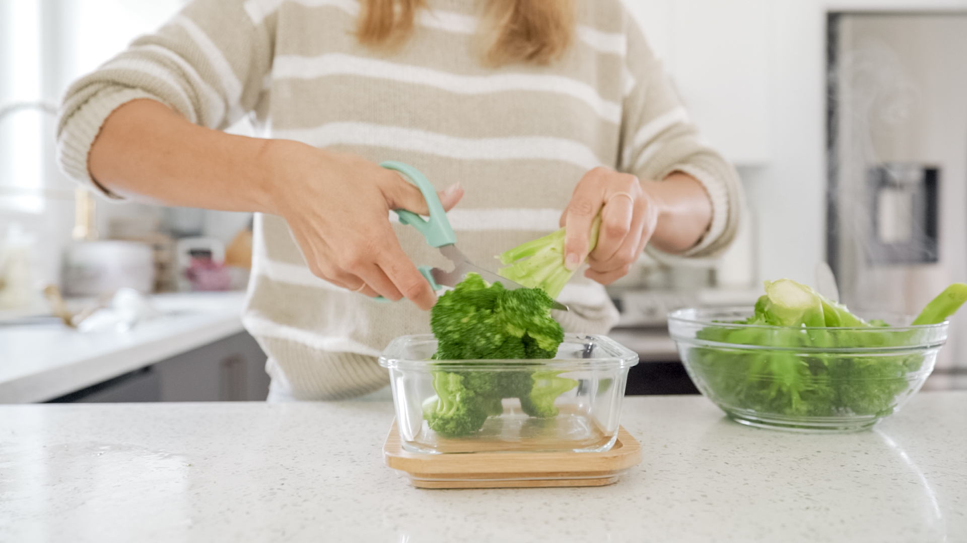 woman in kitchen cutting broccoli with scissors 