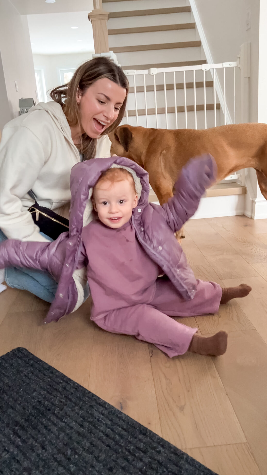 A woman helping a toddler put on her purple jacket