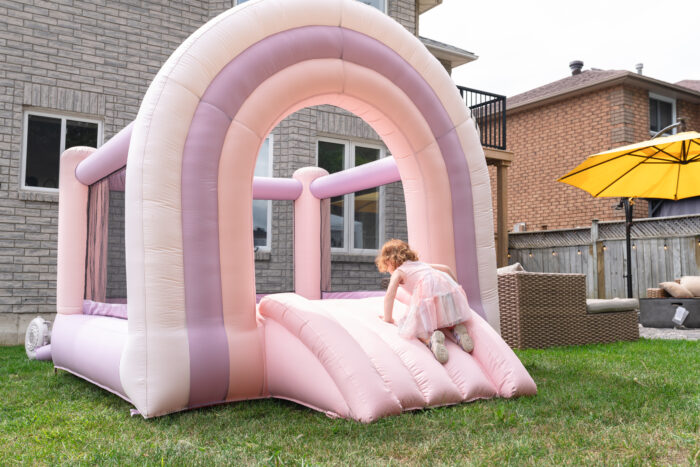 A pink bounce castle with a little girl in a pink dress crawling inside.